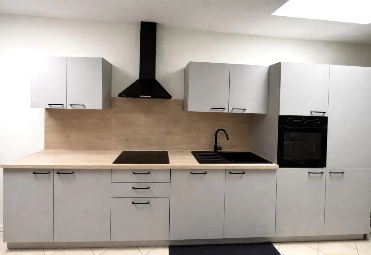 Cuisine équipée aux façades gris clair avec plan de travail et crédence effet bois, hotte noire
