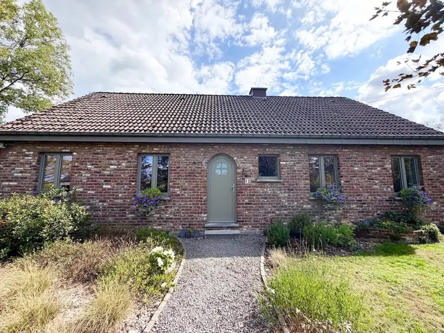 Maison en briques avec châssis gris et porte d’entrée cintrée vert sauge