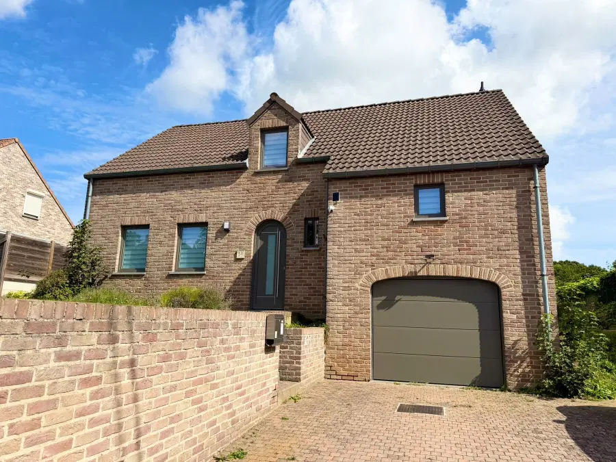Maison en briques avec porte de garage sectionnelle, porte d’entrée cintrée et châssis