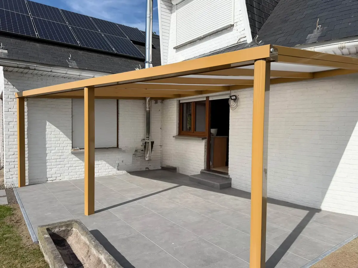 Pergola aluminium teinte ocre couvrant une terrasse carrelée devant une maison en briques blanches