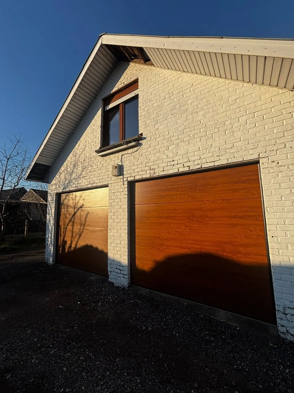 Deux portes de garage sectionnelles teinte bois posées par Arena Invest sur une maison en briques claires