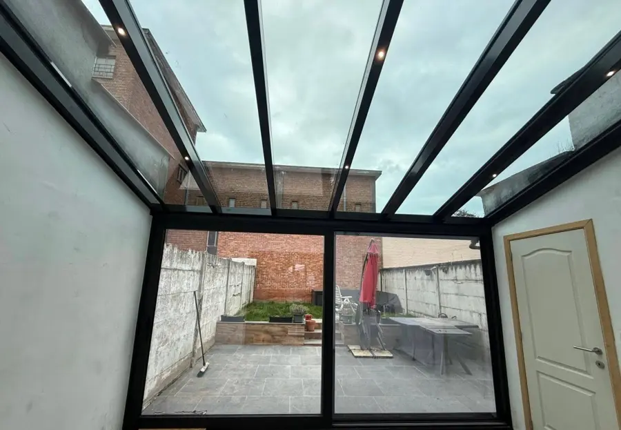 Intérieur d’une véranda à ossature noire et toiture vitrée donnant sur la cour