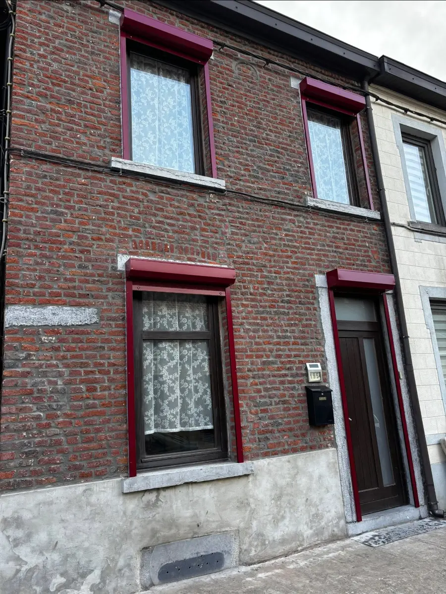 Façade en briques rouges équipée de volets roulants bordeaux aux fenêtres et à la porte d’entrée